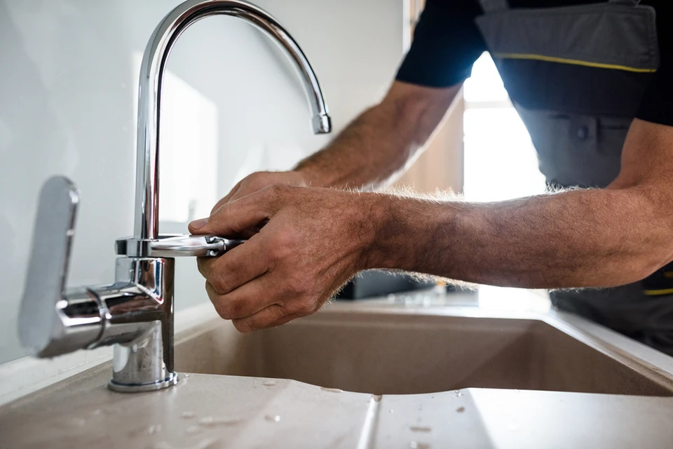 Gros plan sur les mains d'un réparateur âgé en uniforme travaillant, réparant le robinet de cuisine cassé à l'aide d'une clé réglable